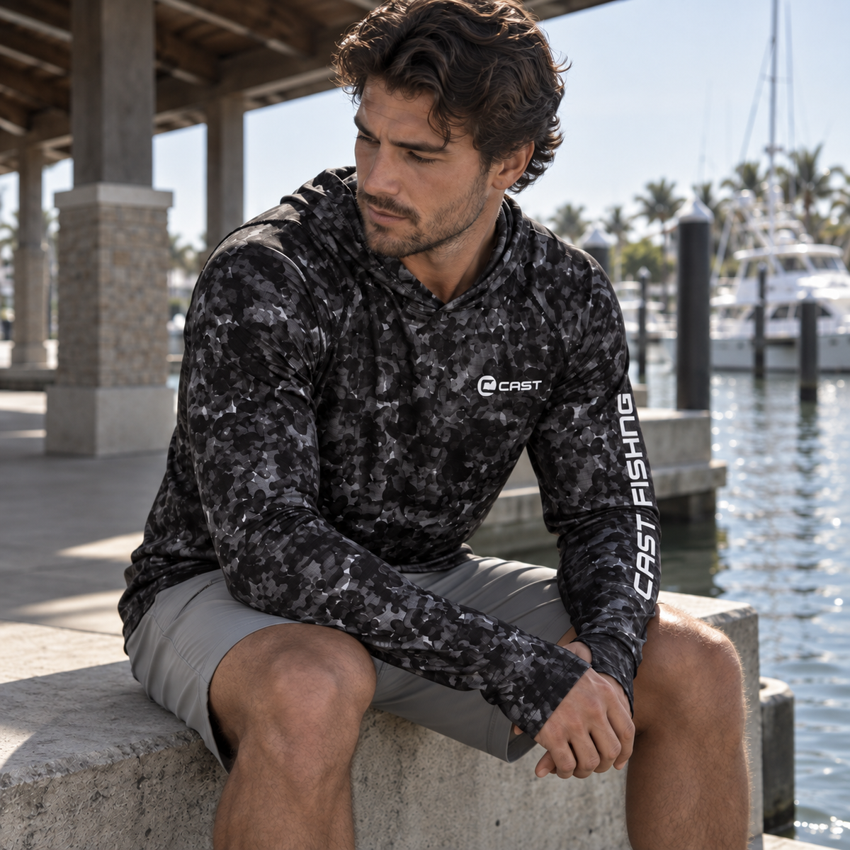 Man seated at the waterfront in the Black Aqua BreezeTec hooded shirt